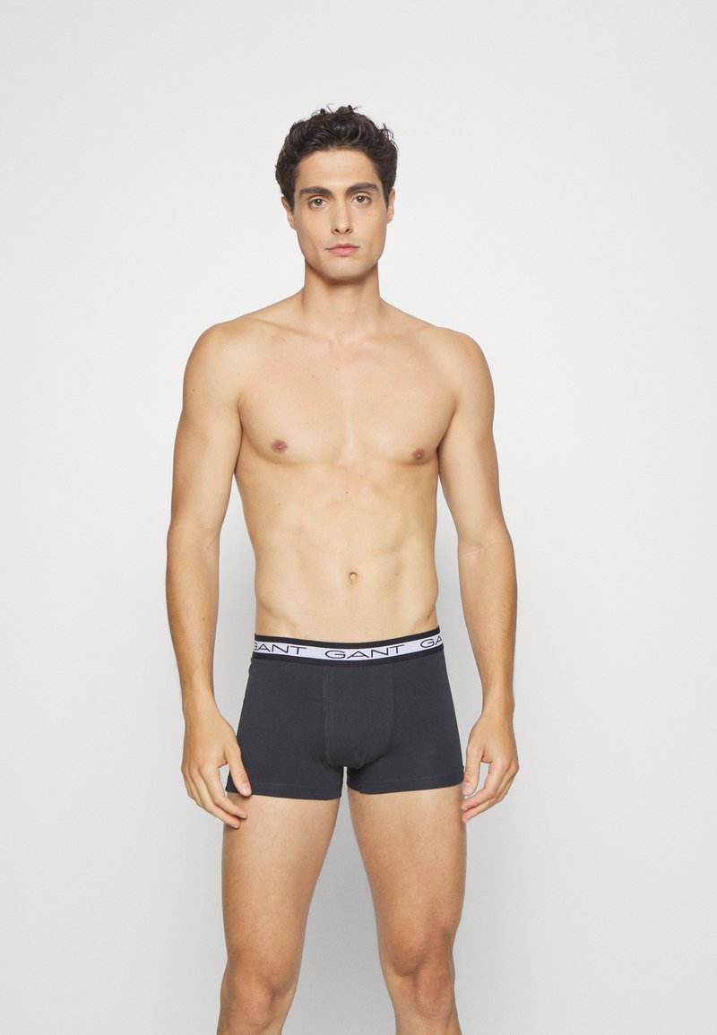 Black cotton boxer briefs with a white band featuring the brand name "GANT" repeated around the waist. Simple design, snug fit.