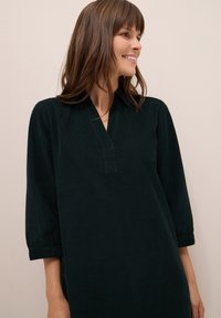 Tumma vihreä corduroi-mekko, jossa on kauluskanta, kolmannekselle hihoille ja hienovaraisia ompelutuksia. Pehmeä kangas ja rento istuvuus.