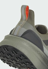 Ultraboost runner shoe in green with textured fabric, a gray accent panel, black rubber sole, and orange pull tab. Features a robust design.