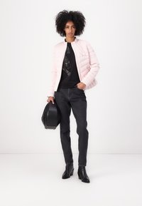 Light pink quilted jacket, black graphic t-shirt, dark jeans, and black heeled boots. Accessories include a black handbag.