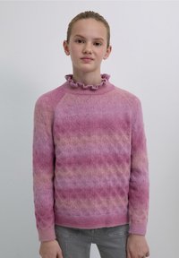 Jersey de punto en tonos degradados de rosa con un patrón texturizado de diamantes, cuello con volantes y puños acanalados. Vaqueros grises completan el conjunto.