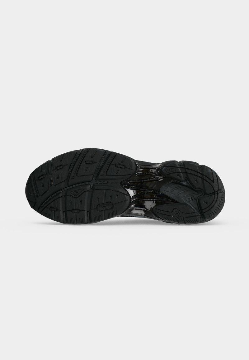 Suela de un zapato deportivo negro que muestra un patrón de dibujo texturizado y un detalle brillante de la entresuela sobre un fondo claro y liso.
