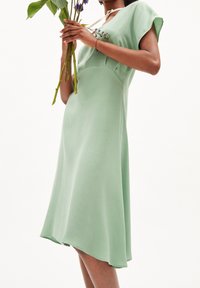 Płynna, miętowa sukienka z okrągłym dekoltem i krótkimi rękawami, wyróżniająca się miękką fakturą i korzystnym, A-liniowym krojem.