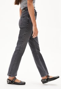 Grijze high-waisted jeans met een rechte pijp, gecombineerd met zwarte platte schoenen met zilveren studs op de band.