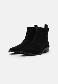 Stivaletti neri in suede con punta affilata, tacco impilato e linguette per indossarli facilmente. Texture liscia e elementi di design minimalisti.