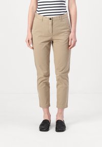 Beige slim-fit bukser med knaplukning, sidelommer og opsmøg ved anklerne, i kombinasjon med sorte loafers og en stribet top.
