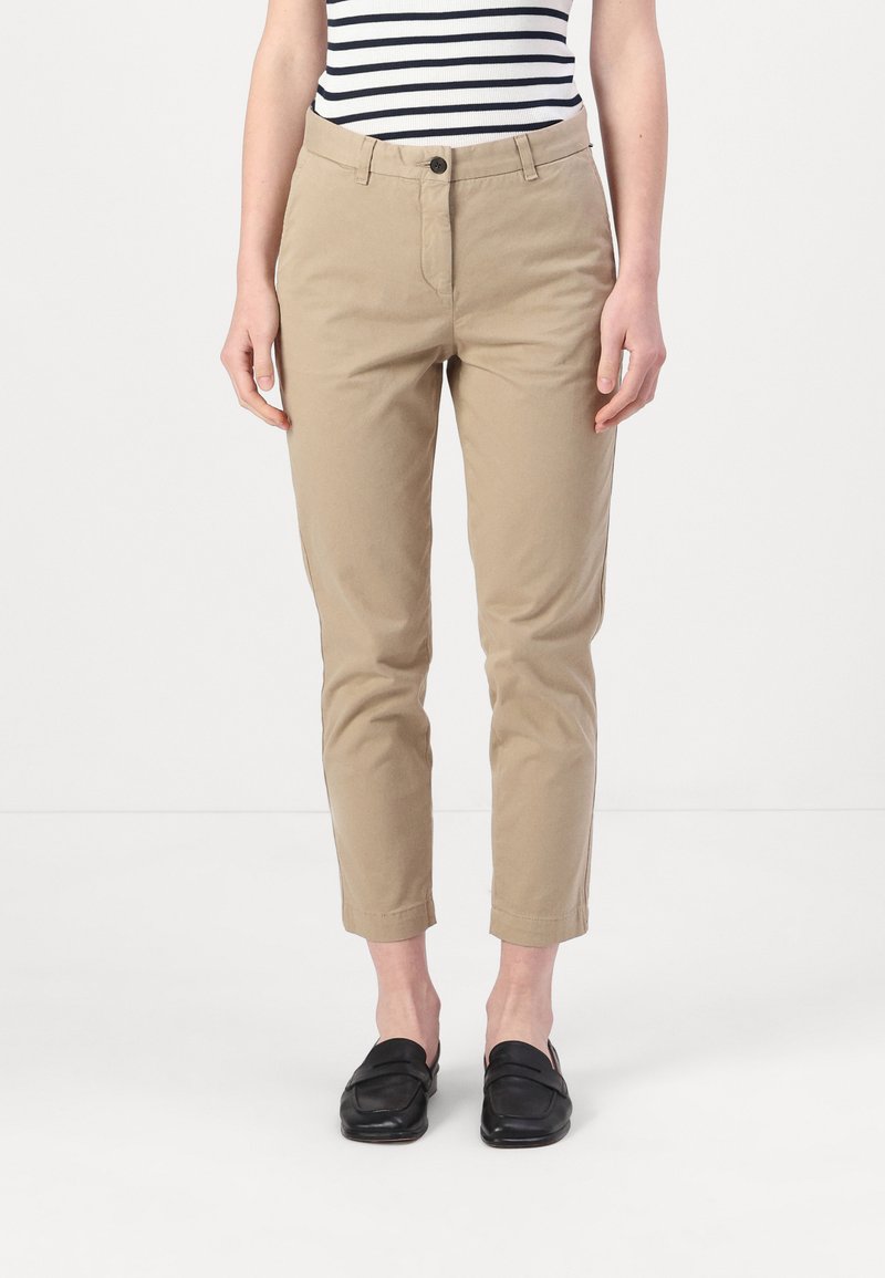 Beige slim-fit bukser med knaplukning, sidelommer og opsmøg ved anklerne, i kombinasjon med sorte loafers og en stribet top.