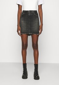 Černá denimová mini sukně s třepeným lemem, umístěná do poloviny stehna, spárovaná s černými kotníkovými botami a bílým tričkem.