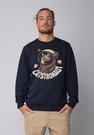Marineblaues Sweatshirt mit einem Grafikdesign von einer Katze in einem Astronautenhelm und Planeten. Das Design enthält beigen Text mit der Aufschrift "CATSTRONAUT."