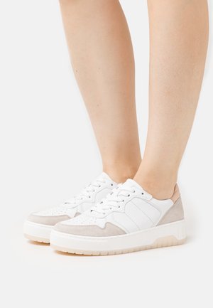 White and beige sneaker featuring a smooth leather body, suede accents, perforated details on the toe, and a rubber sole with textured grip.