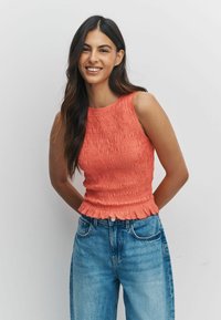 Korallivärvi varrukateta topp tekstuurse triibutusega, volangidega alumise äärega, kombineeritud kõrge vöökohaga siniste teksapükstega, mis on lõdva istuvusega ja kulunud detailidega.