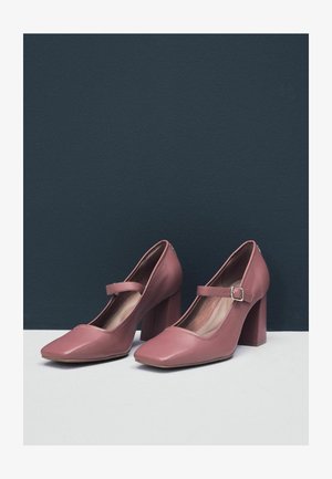 Rózsaszín műbőr Mary Jane sarkú cipők négyzetes orral, széles tömbsarkal és állítható pánttal rendelkeznek, amelyhez kis fémszegély tartozik.