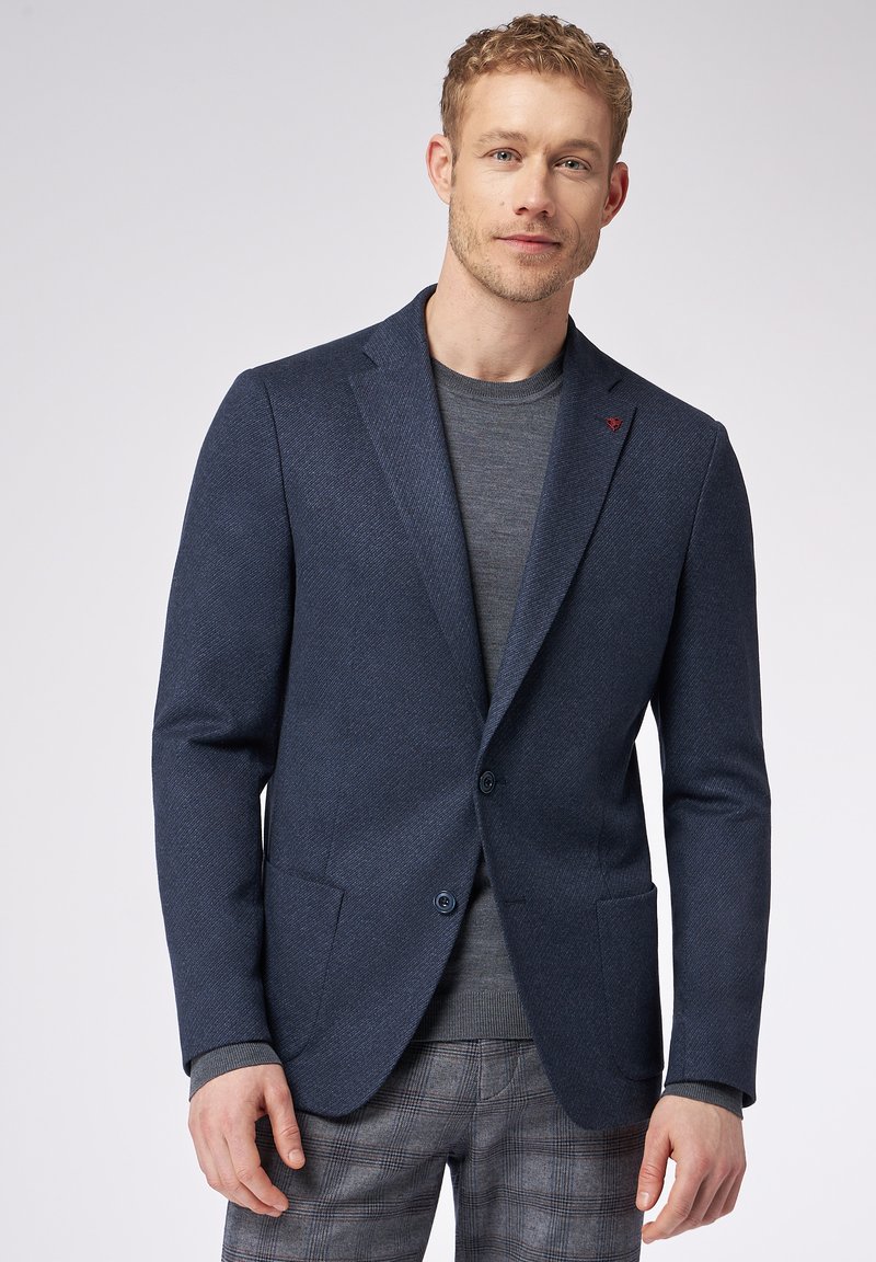 Blazer blu navy in tessuto testurizzato, a un petto con due bottoni, abbinato a una maglietta grigia a girocollo e pantaloni grigi a quadri.