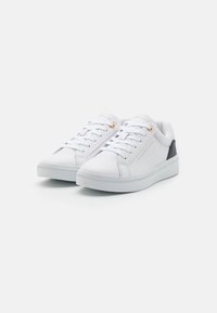 Zapatillas de cuero blanco con un acabado suave, con punta redondeada, suela blanca plana y detalles en negro en el talón. Detalle de ojete dorado.
