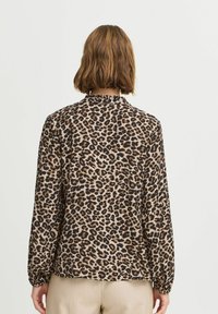 Blusa con stampa leopardata, tessuto leggero, colori nero e marrone chiaro, maniche lunghe con polsini arricciati, colletto alto e vestibilità comoda.