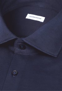 Chemise bleu foncé à col avec boutons et étiquette de marque "seidensticker" cousue à l'intérieur de l'encolure.