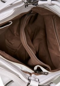 Wnętrze białej skórzanej torebki, pokazujące brązową tkaninę wyściółki, dwie zamykane na zamek przegrody oraz przestrzeń centralną. Widoczne zamki błyskawiczne i szwy.