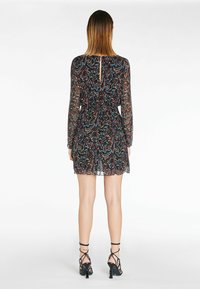 Schwarzes, durchsichtiges Kleid mit buntem Paisley-Muster, langen Ärmeln und Bindeband in der Taille. Mit einem Ausschnitt am Rücken und gewelltem Saum.