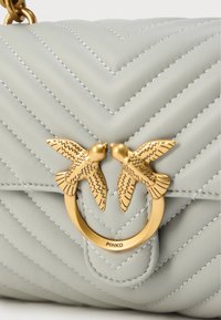 Γκρι δερμάτινη τσάντα με σχέδιο καπιτονέ σε σχήμα σβούρας. Διαθέτει χρυσό κυκλικό μεταλλικό στοιχείο με διπλές λεπτομέρειες πουλιών. Υπέροχες ραφές σε όλη την επιφάνεια.