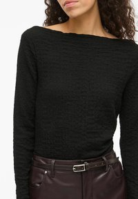 Czarna, teksturowana bluzka z długim rękawem i szerokim dekoltem, zestawiona z dopasowanymi brązowymi skórzanymi spodniami z paskiem i bocznymi kieszeniami.