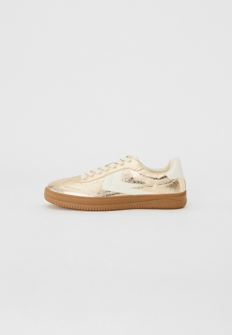 Sneaker metallici oro con tomaia texturizzata, accenti bianchi e suola in gomma marrone. Presentano un classico sistema di allacciatura e una forma arrotondata.