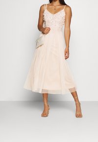 Rosa Midi-Kleid mit verziertem Oberteil, Spaghettiträgern und Tüllrock; kombiniert mit einer strukturierten cremefarbenen Umhängetasche und Riemchensandalen.