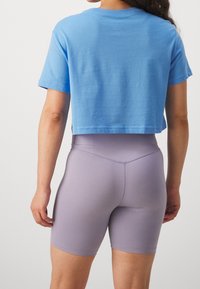 Avskuren blå bomullströja med korta ärmar, matchad med högmidjade lavendelfärgade leggings. Slät textur och figurnära design.