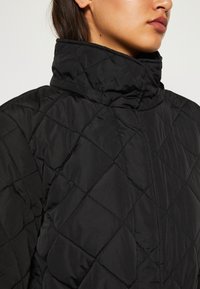 Giacca nera trapuntata con colletto alto, caratterizzata da un motivo a diamante e una texture liscia, ideale per calore e comfort.