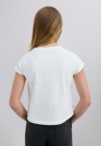 Camiseta blanca de manga corta con cuello redondo y corte recto, combinada con pantalones negros. Tejido de algodón suave con un ligero brillo.
