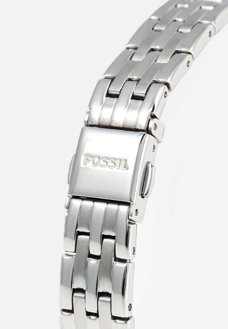 Reloj de pulsera de metal plateado con diseño de pulsera articulada. Presenta un acabado pulido y un cierre grabado con "FOSSIL."