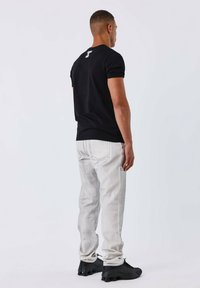 Maglietta nera a maniche corte con logo sul retro, abbinata a jeans grigi chiari e sneakers nere. Design semplice con vestibilità su misura.