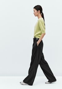 Maglione in misto lana verde, pantaloni neri a gamba larga con tasche e scarpe argento. Design semplice, texture liscia e sottile contrasto di colore.