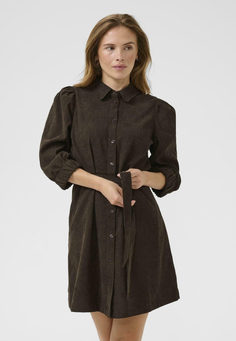Robe brune à boutons avec un col, des manches bouffantes et une ceinture assortie. Fabriquée en tissu texturé, elle présente une coupe décontractée et une longueur mi-genou.
