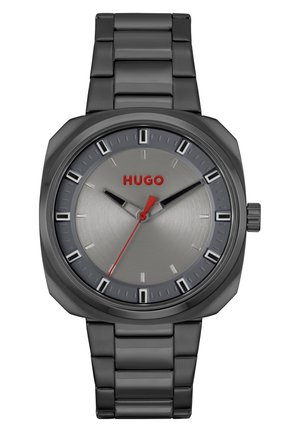 Die schwarze Metall-Uhr verfügt über ein graues Zifferblatt mit silbernen Stundenmarkierungen und einem roten Logo. Ein kontrastierender roter Sekundenzeiger ergänzt das elegante Design.
