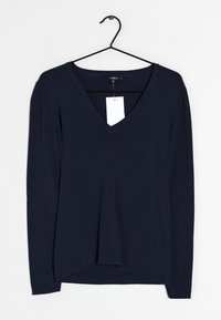 Mörkblå långärmad V-ringad tröja med avslappnad passform, med en etikett, en rundad fåll och mjukt, lätt tyg. Hänger på en svart krok.