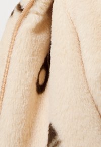 Primo piano di tessuto in pelliccia sintetica color crema morbido con macchie marrone scuro irregolari e una cucitura visibile.