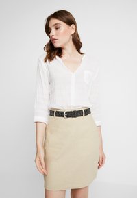White, textured button-up shirt with a v-neck and long sleeves; beige skirt with a straight cut; black leopard-print belt with a silver buckle.