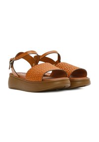 Sandali in pelle intrecciata marroni con punta aperta, cinturini incrociati e suola a zeppa bassa. Presenta una chiusura con fibbia robusta di lato.
