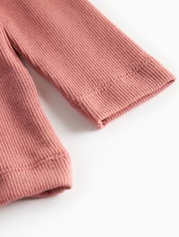 Close-up of pink ribbed fabric sleeves with visible stitching on a white background.