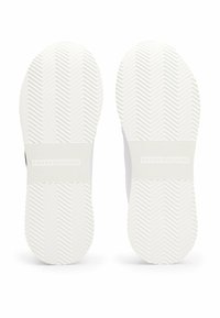 Solle di sneaker bianche con un motivo a spina di pesce, nome del brand impresso e una fascia centrale testurizzata per grip e durata.
