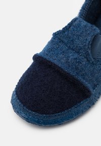 Blue felt slip-on shoe with a dark blue toe cap, textured upper, elastic side, and a sturdy rubber sole. Close-up view.