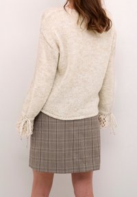 Kremowy sweter dzianinowy z szerokimi rękawami, ozdobiony koronkowymi sznurkami. W połączeniu z brąskowymi, w kratę spódnicą, podkreślającą dopasowaną sylwetkę.