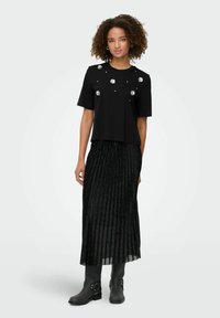 Sort kortærmet top med sølvfarvede blomsterdekorationer, parret med en plisseret sort nederdel med glitrende detaljer og knæhøje sorte støvler.