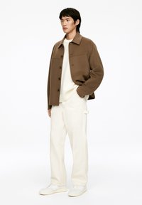 Braune Wollmischungjacke mit Kragen, Knopfverschluss, cremigem Strickpullover, weißen Hosen und weißen Sneakers. Einfaches, strukturiertes Design.