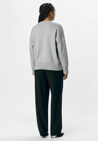 Grå sweater med en afslappet pasform, ribbet kant og lange, brede ærmer, parret med sorte bredde-buks og spidse sorte sko.