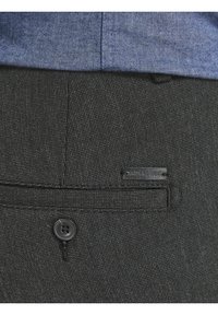 Svarta texturerade byxor med en bakficka, prydd med en svart knapp och en liten tygetikett märkta "JACK & JONES" nära fickan.