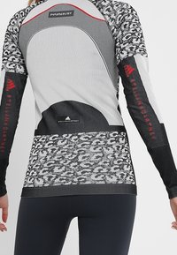 Pitkähiha sporToppi harmaana ja mustana. Ominaisuuksiin kuuluu teksturoitu leopardikuvio, kontrastiväriset saumat ja logoviritelmät hihoissa ja selässä.