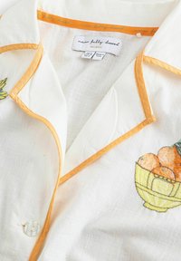 Balti mygtukais užsegama marškiniai su oranžinėmis detalėmis ir siuvinėtu vaisių krepšelio motyvu. Minkšta, lengva medžiaga, su klasikiniu apykakliu ir skaidriais mygtukais.