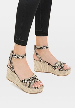 Kilesandaler med slangeskindsmønster i sort og beige, med krydsede stropper og sål med platform indpakket i jute.
