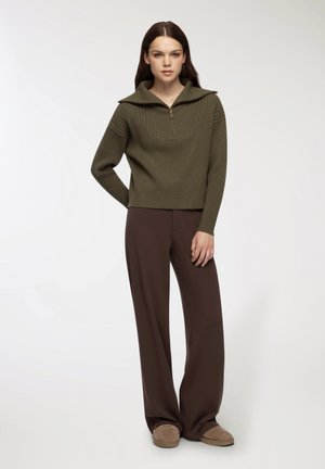 Maglione a coste verde oliva con colletto zip, abbinato a pantaloni larghi marroni e scarpe slip-on beige. Design e vestibilità semplici e puliti.